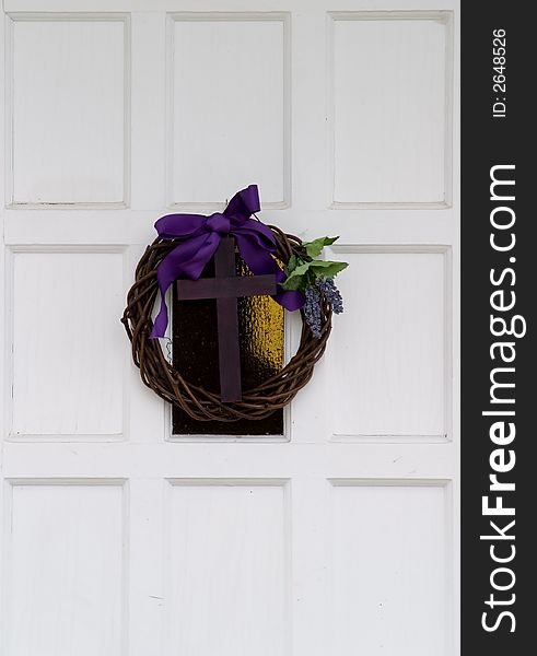 Wood cross hanging on a white door with a purple ribbon and a wreath. Wood cross hanging on a white door with a purple ribbon and a wreath