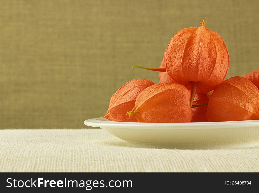 White plate with orange fruits on brown background. White plate with orange fruits on brown background