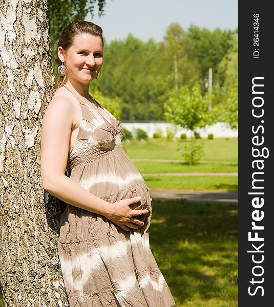 A pregnant girl is standing at the tree in nature