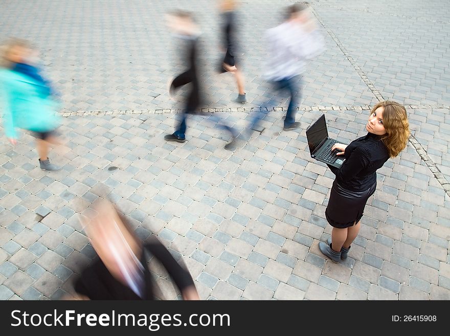 Young attractive businesswoman working on laptop through wireless technology. Motion blurred commuters walking to work