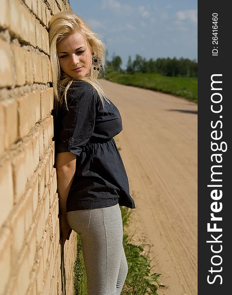 Beautiful blonde girl is standing against the wall on the nature