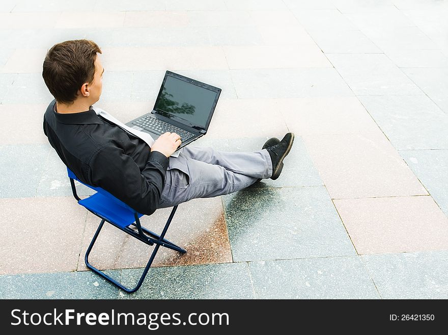 Image of the businessman using the laptop in the empty street. Focus is made on top of the background color tile in the street. Image of the businessman using the laptop in the empty street. Focus is made on top of the background color tile in the street.