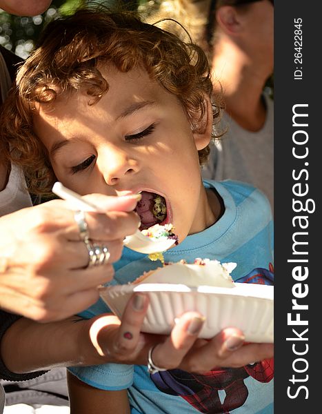 A young boy eating a cake with mom