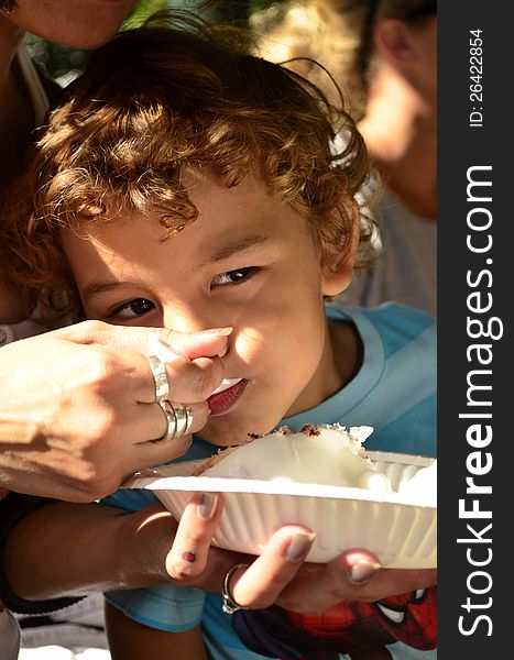 A young boy eating a cake with mom