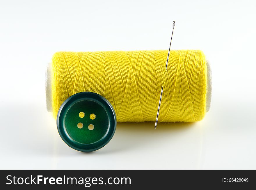 Yellow spool of thread and a green button  on white background. Yellow spool of thread and a green button  on white background