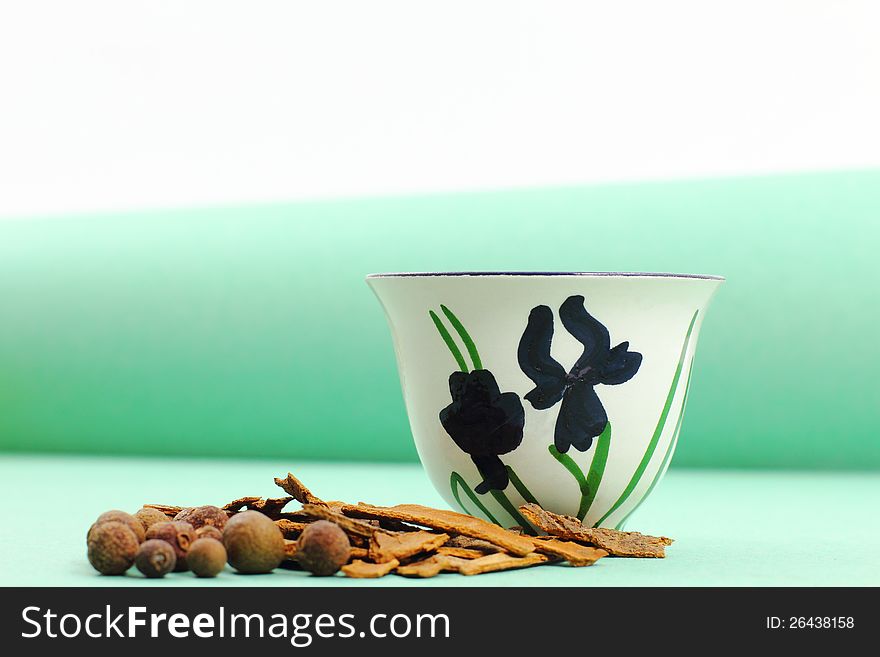 A green-themed Arabic coffee cup with a green backdrop and cinnamon sticks as well as spices in front. The scheme is hand-drawn.