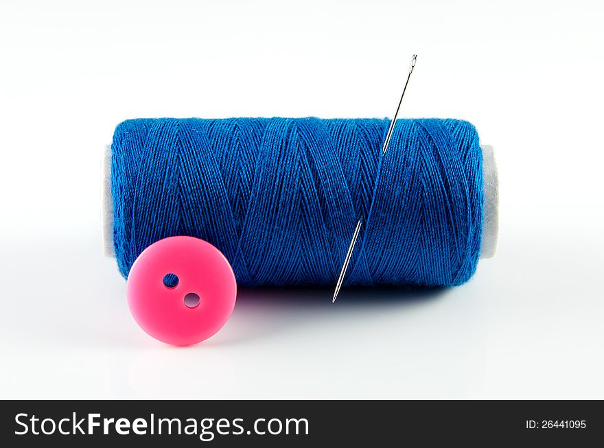 Blue spool of thread and a pink button isolated on white background. Blue spool of thread and a pink button isolated on white background