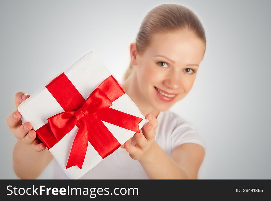 Beautiful young woman with a Christmas gift with red ribbon in their hands on a gray background. Beautiful young woman with a Christmas gift with red ribbon in their hands on a gray background