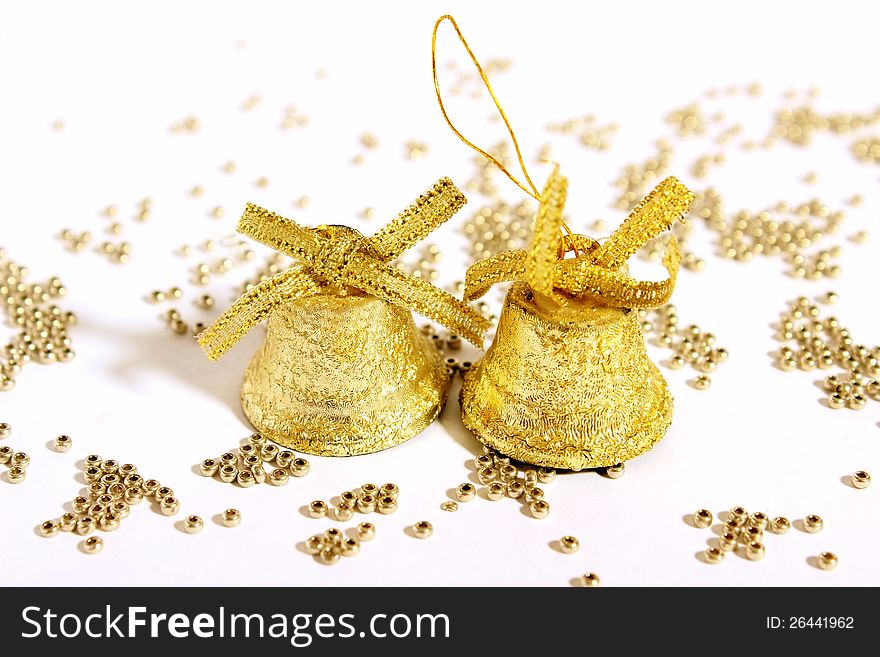 Against the background of golden beads scattered two Christmas Christmas gold bells with bows. Against the background of golden beads scattered two Christmas Christmas gold bells with bows