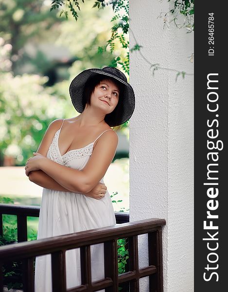 Girl in a white dress and black hat posing on the balcony. Girl in a white dress and black hat posing on the balcony