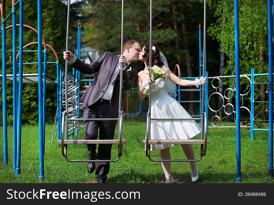 Romantic kiss bride and groom on swing in summer park