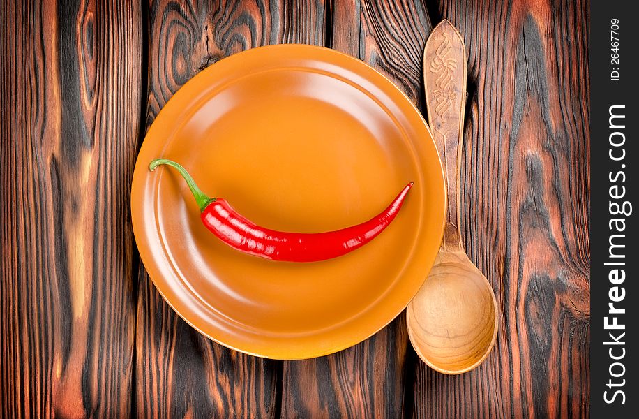 Pepper in a plate and spoon on a wooden background