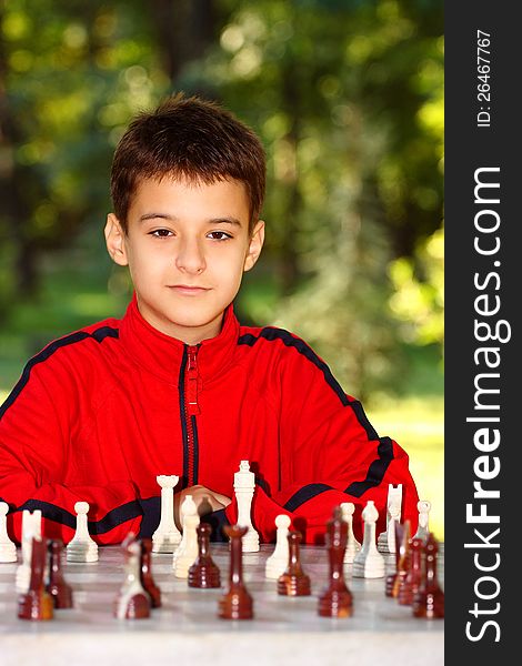 A boy looking at the camera playing chess outdoor in green park. A boy looking at the camera playing chess outdoor in green park