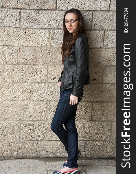 Girl leaning against a wall, wearing a leather jacket and jeans. Girl leaning against a wall, wearing a leather jacket and jeans