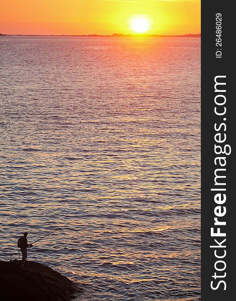 Angler at the coast of Brittany with the rising sun in the background