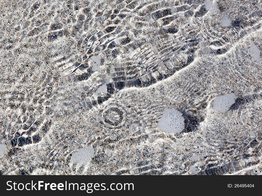 Background texture with water ripples at the seafront, with the sand of the beach shining through the flat water. Background texture with water ripples at the seafront, with the sand of the beach shining through the flat water