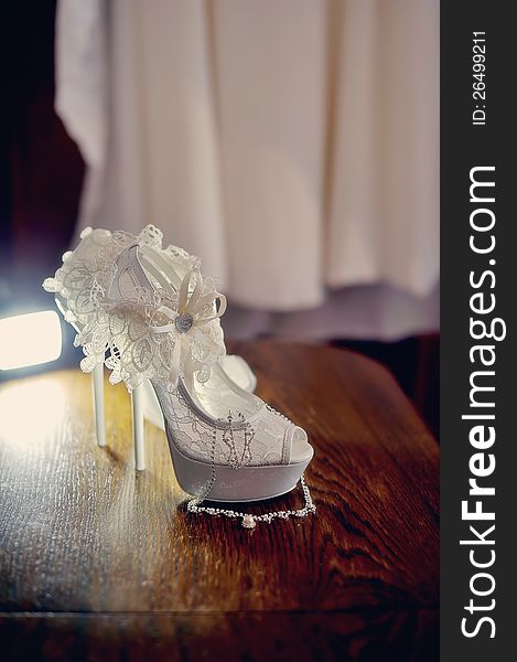 On the wooden floor are white shoes for the bride with dressing. On the wooden floor are white shoes for the bride with dressing