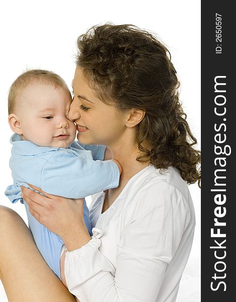 Young happy mother hugging baby. Woman is sitting in bed, baby is sitting on her. White background. Young happy mother hugging baby. Woman is sitting in bed, baby is sitting on her. White background