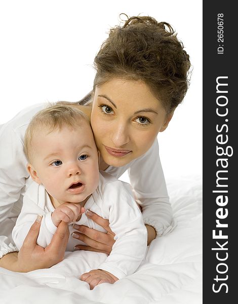 Young happy mother holding baby. Woman is lying in bed, holding baby. White background, looking at camera. Young happy mother holding baby. Woman is lying in bed, holding baby. White background, looking at camera