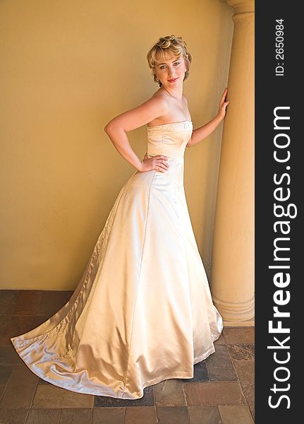 Beautiful blond bride with short hair in beige pearl dress leaning against a pillar. Beautiful blond bride with short hair in beige pearl dress leaning against a pillar