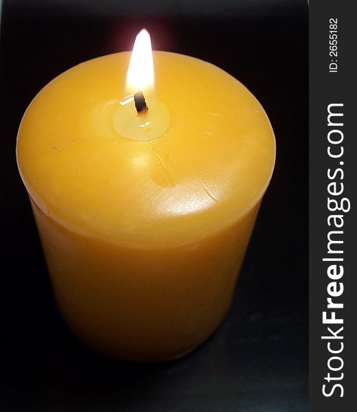Orange lighted candle on black background.