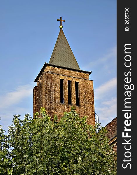 Old red brick church tower with iron cross.