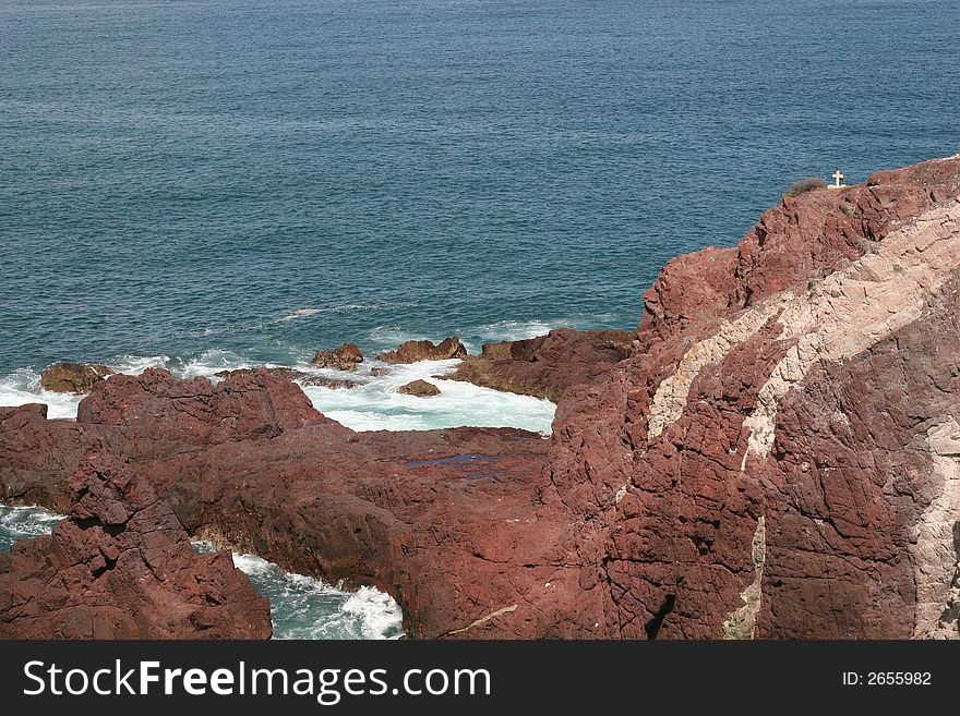 Rocky cliffs leading to sea with a cross at the edge. Rocky cliffs leading to sea with a cross at the edge