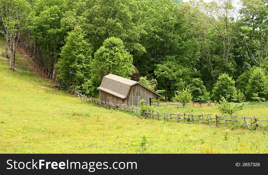 An old barn and rail fence nestled in a grassy mountain knoll. An old barn and rail fence nestled in a grassy mountain knoll