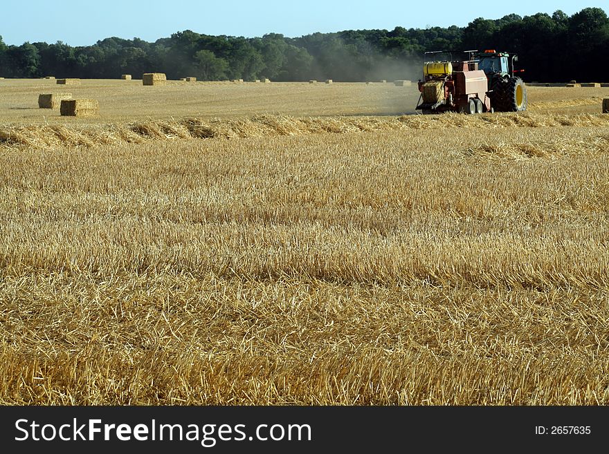 This is an image of a tractor and baler in a wheat field. This is an image of a tractor and baler in a wheat field.