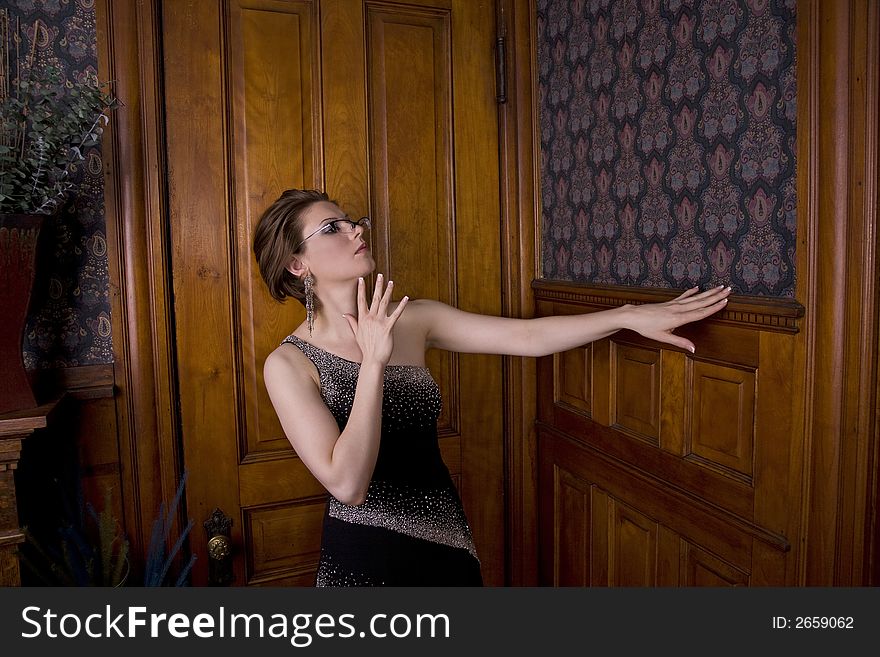 Beautiful young brunette woman in an evening gown looking critically at the woodwork on a wall. Beautiful young brunette woman in an evening gown looking critically at the woodwork on a wall.