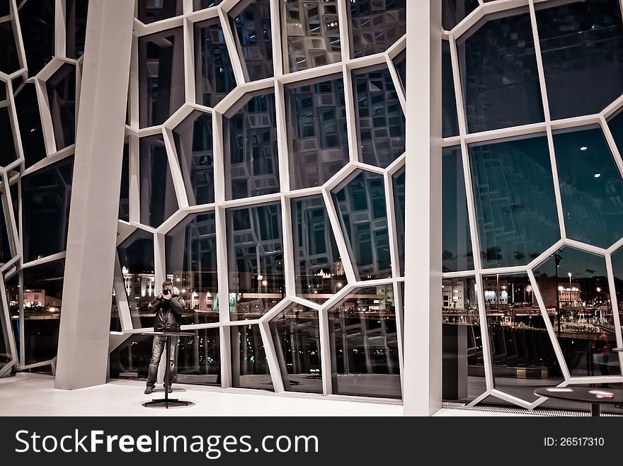 Man taking photo inside of glass house. Reykjavík city is in the background