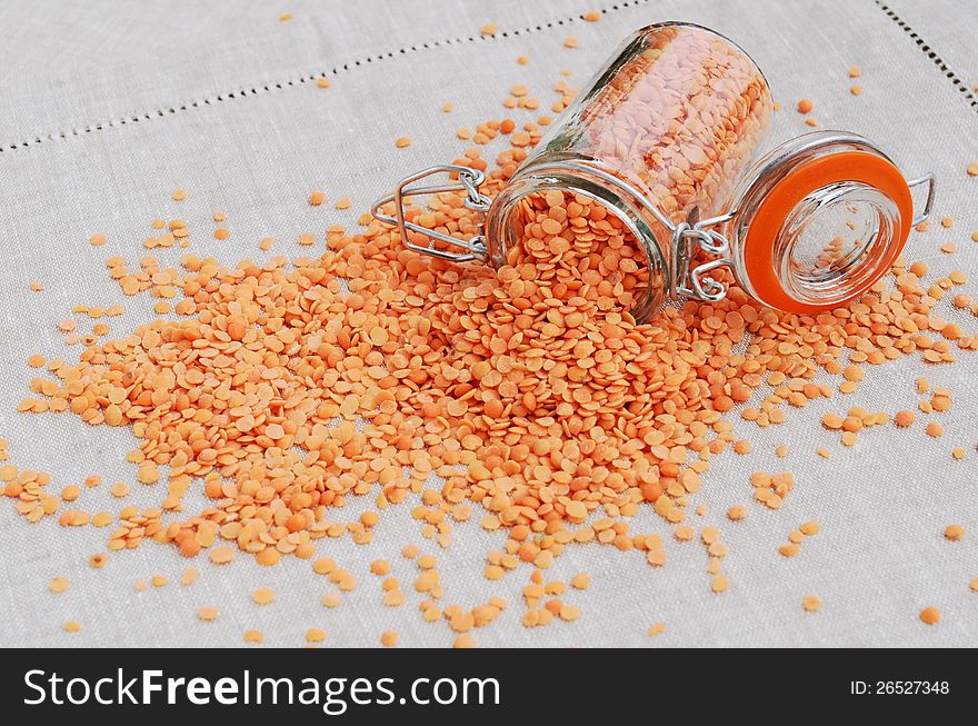 Red lentils spilled out from jar on grey linen table napkin. Red lentils spilled out from jar on grey linen table napkin