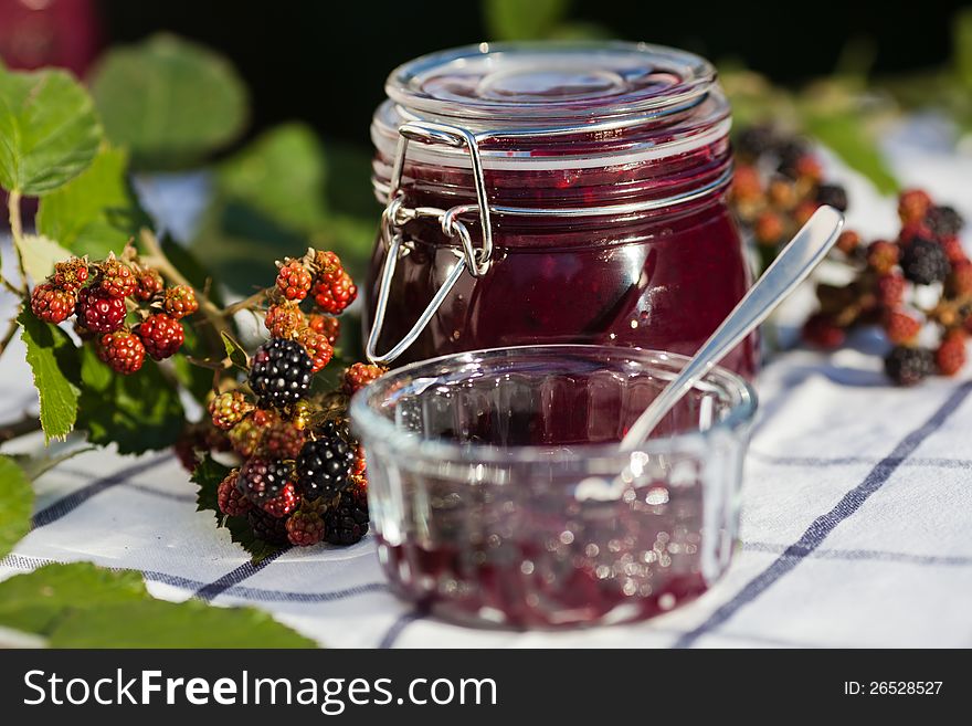 Self-made blackberry jam in a jam jar and a bowl, decorated with a fresh blackberry branch