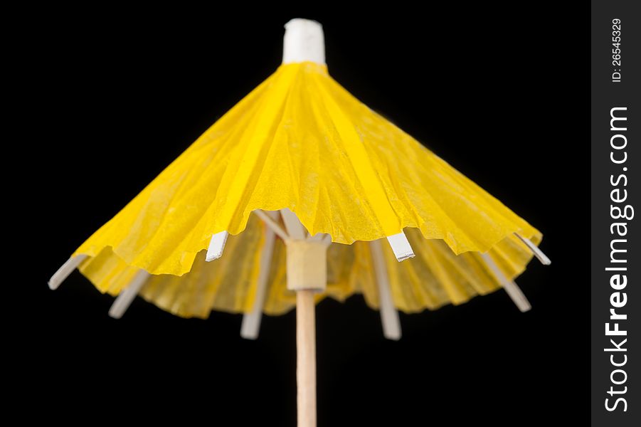 A bright yellow cocktail umbrella with a toothpick on black background. A bright yellow cocktail umbrella with a toothpick on black background