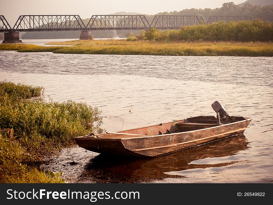 Flat- bottom boat floating slightly offshore on a river with a railroad bridge in the background. Flat- bottom boat floating slightly offshore on a river with a railroad bridge in the background.