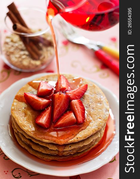 A stack of pancakes with fresh strawberries and syrup pouring over