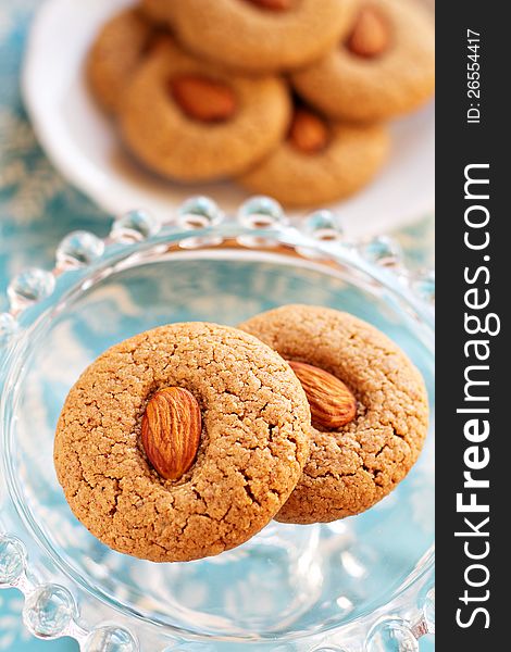 Two almond whole wheat cookies on a small glass cake stand with more cookies in the background