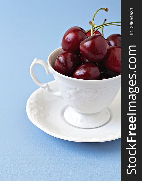 Sweet cherries in a white cup on a light blue background