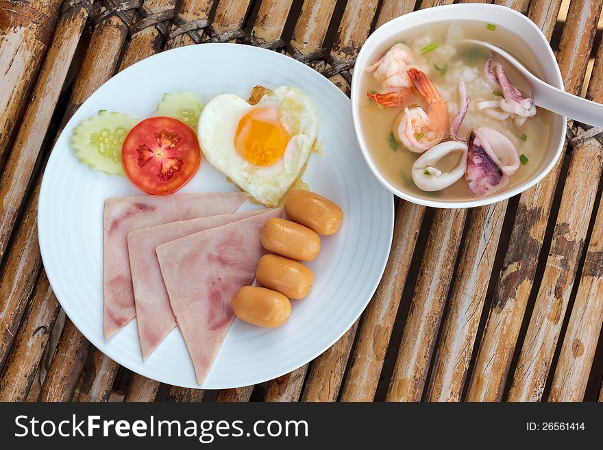 Plate with classic fried egg,ham, sausage and asia soup with seafood breakfast on a bamboo table. Plate with classic fried egg,ham, sausage and asia soup with seafood breakfast on a bamboo table