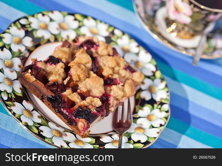 Coffee table with a plum cake on a floral plate and a cup of coffee in the blurred background. Coffee table with a plum cake on a floral plate and a cup of coffee in the blurred background