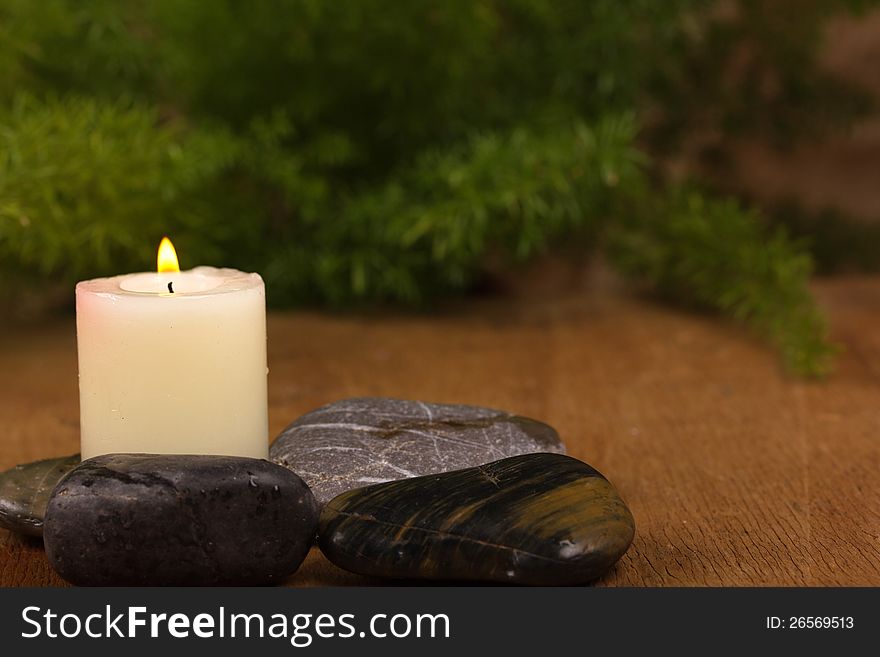 Burning candle and black stones and green leaves on a wooden background. Burning candle and black stones and green leaves on a wooden background