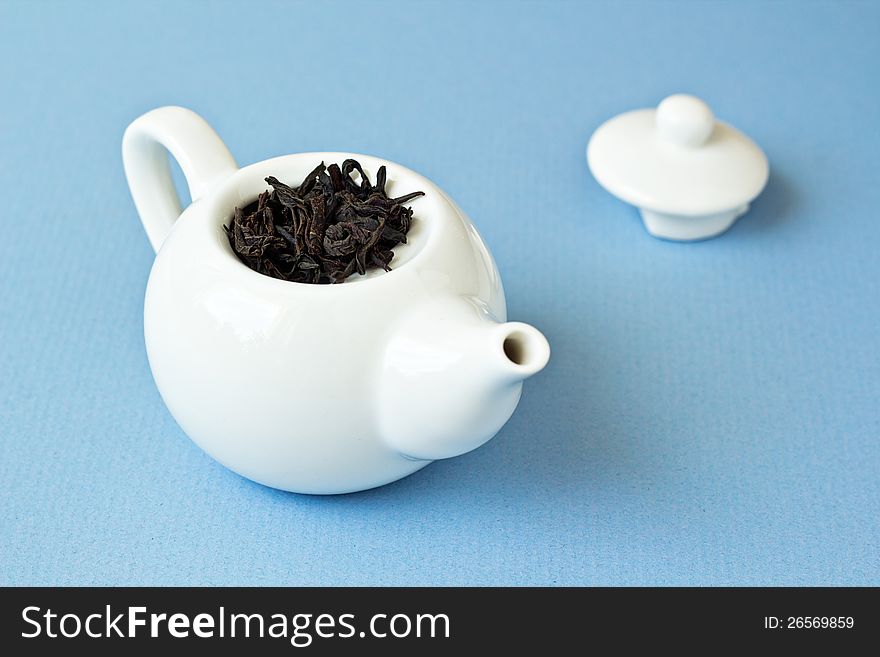 Small tea pot with leaves of black tea on light blue background