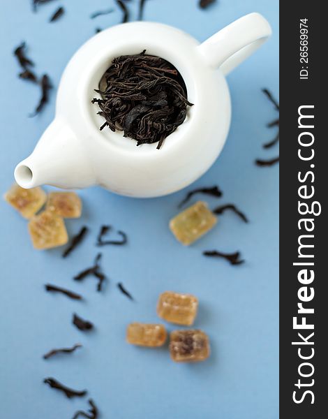 Small tea pot with leaves of black tea, brown crystal sugar on light blue background. Selective focus