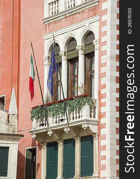 Facade fragment of an ancient building with a balcony, ornaments and flags