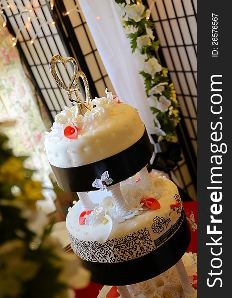 A 3 tier wedding cake on a table with flowers, print and hearts on the top. A 3 tier wedding cake on a table with flowers, print and hearts on the top