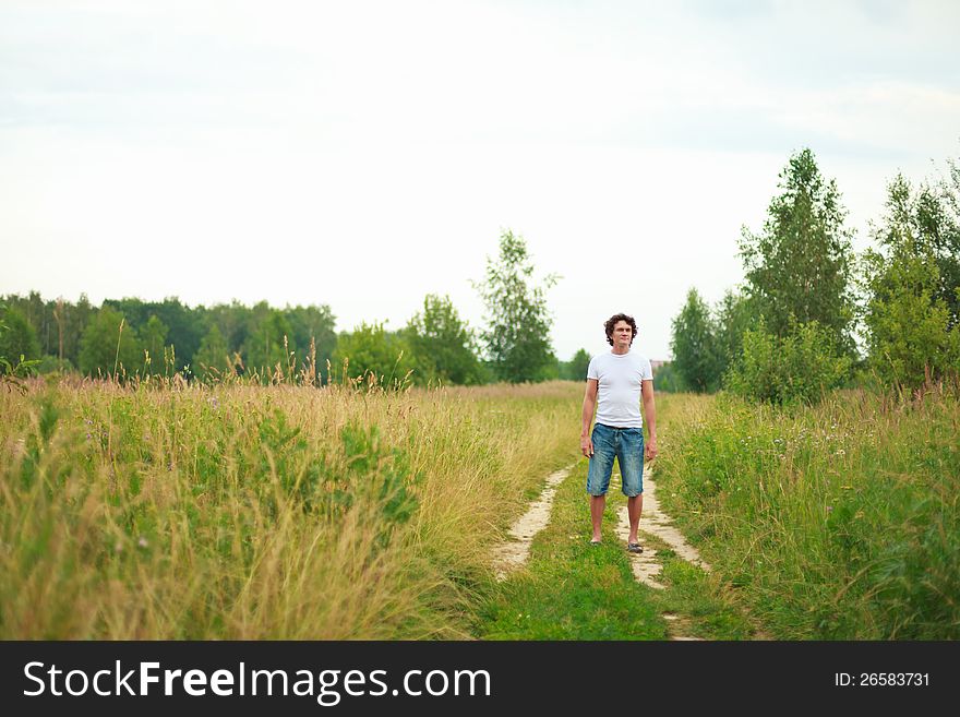 A young man standing on a country road among flowering meadows. A young man standing on a country road among flowering meadows.