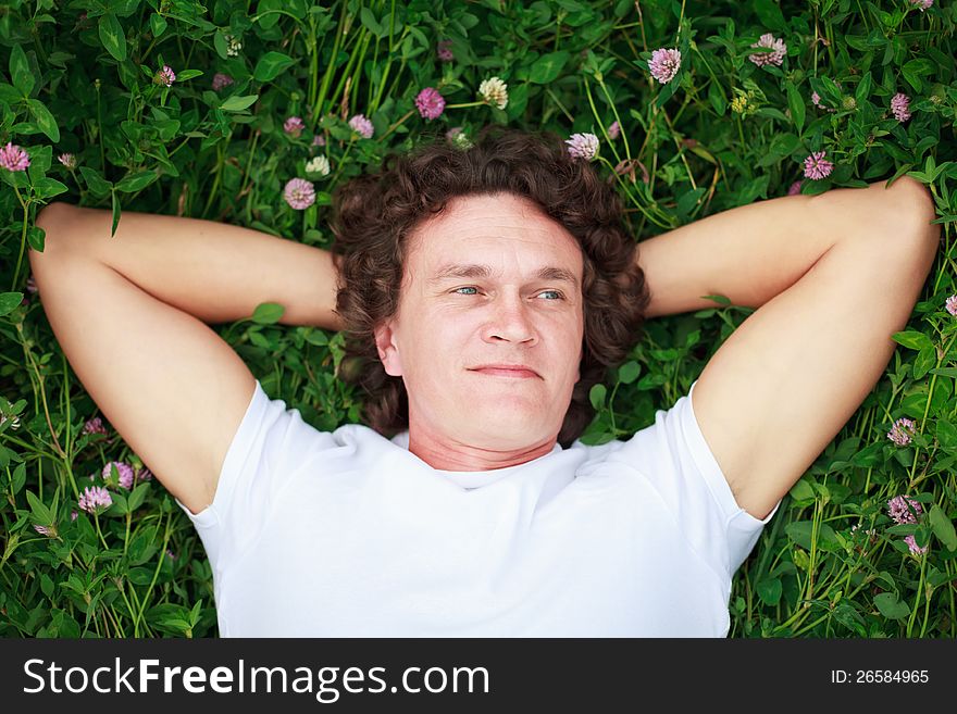 A young man lies on a flowering clover meadow, his hands behind his head. A young man lies on a flowering clover meadow, his hands behind his head.