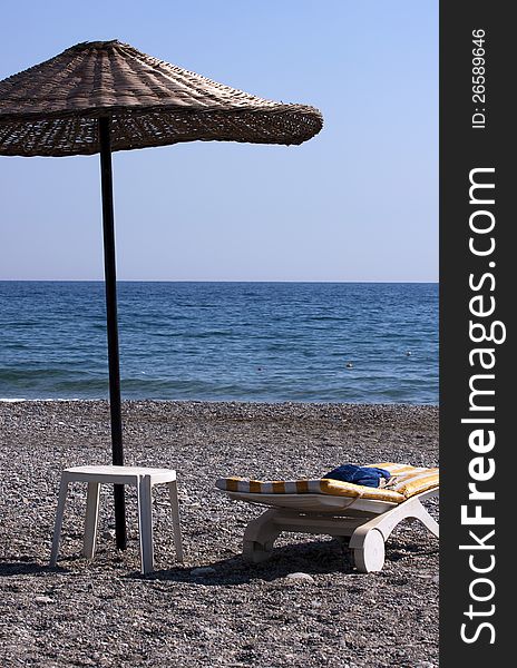 Plastic sun lounger with simple table and a beach umbrella on a deserted beach. Plastic sun lounger with simple table and a beach umbrella on a deserted beach.