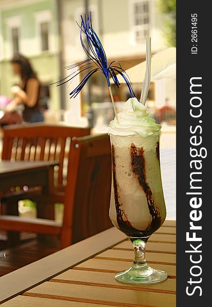 Image of a tasty glass of coffee frappe on a terrace table under a green umbrella which generate some green shadows on the cream. Image of a tasty glass of coffee frappe on a terrace table under a green umbrella which generate some green shadows on the cream.