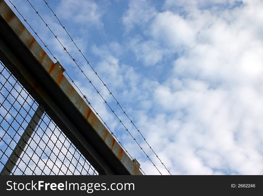 Barbed wire on a rusty fence in front of blue cloudy sky. Barbed wire on a rusty fence in front of blue cloudy sky